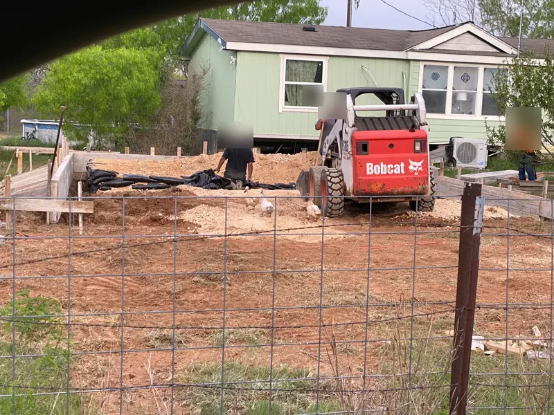 Shop slab prep: wood forms and vapor barrier, a skid steer in the yard.