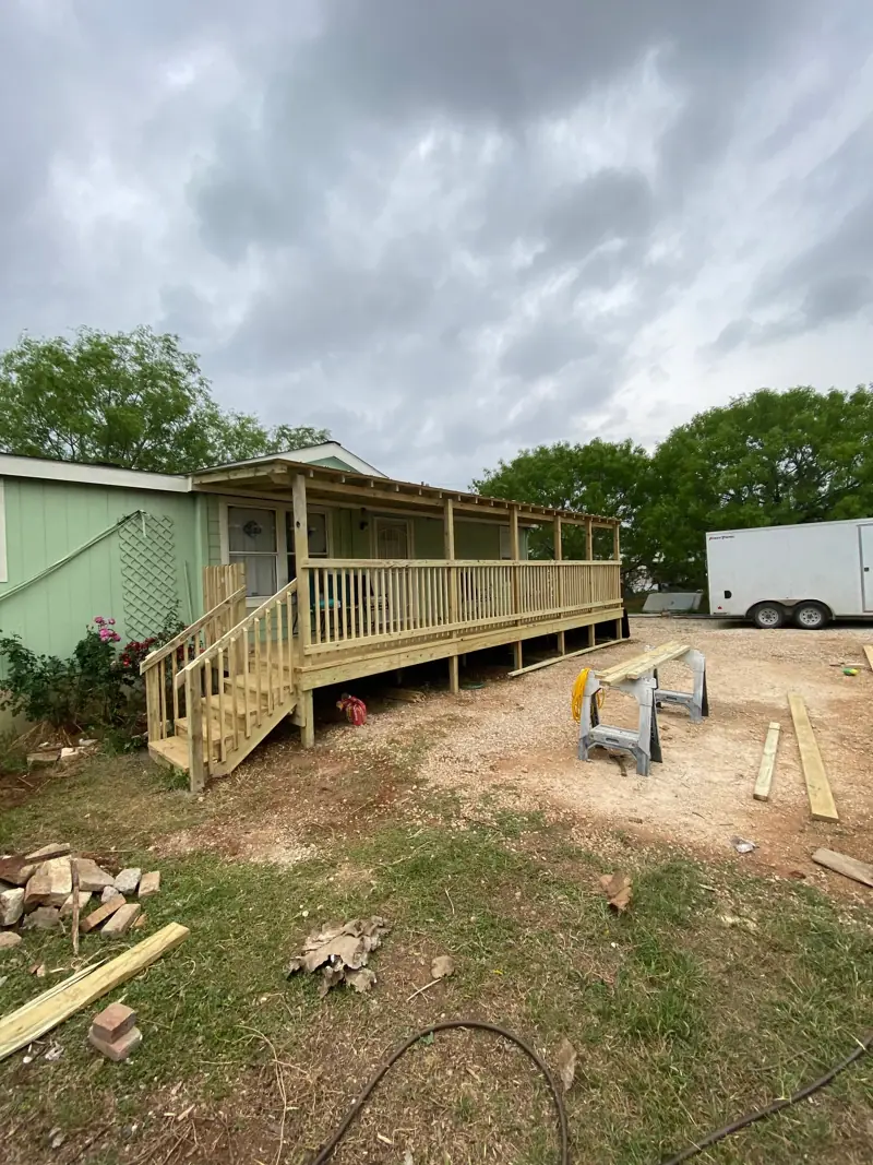 New covered deck with stairs and railing on a green house.