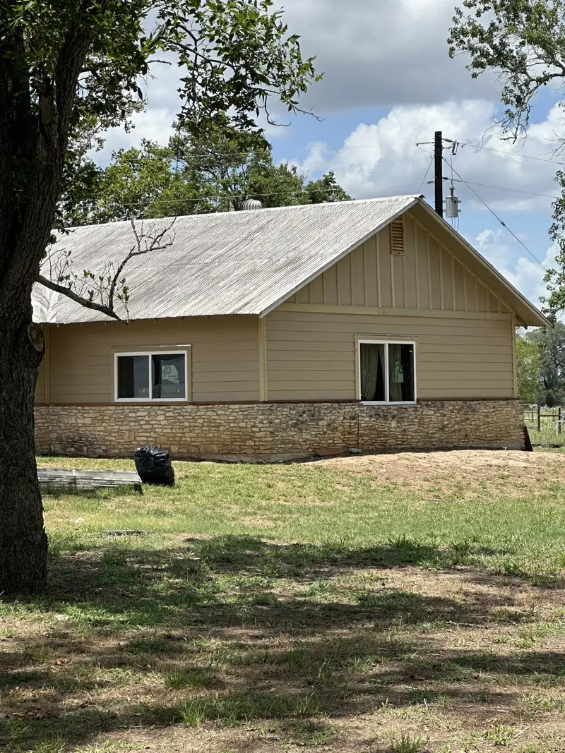 House with tan siding, white windows and a stone base under a metal roof.