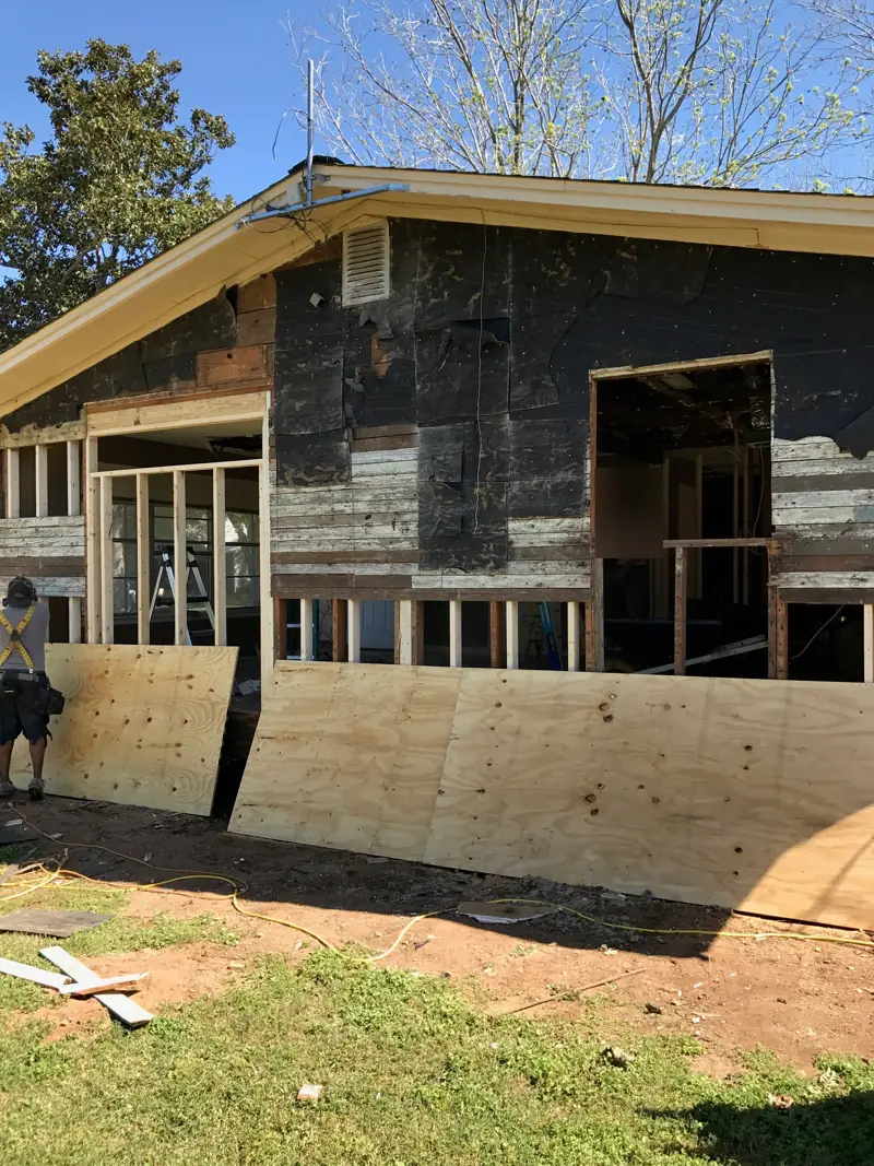 House with the old siding stripped off and new plywood sheathing going on the lower wall.