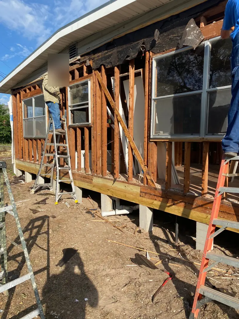 Pier-and-beam house with the old siding stripped to the studs, crew on ladders.