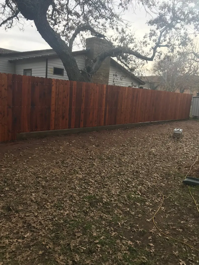 Cedar privacy fence stained red-brown along the back of a yard.