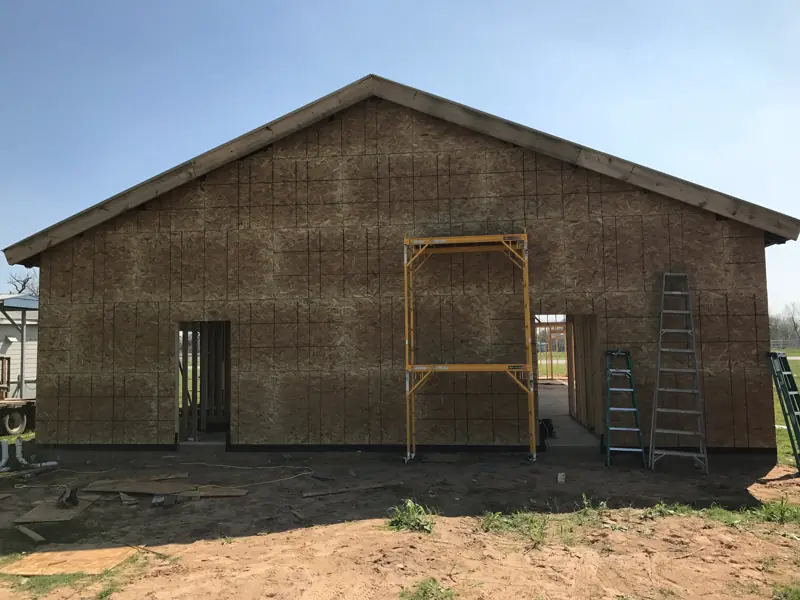 Gable end of the building closed in with sheathing, with door openings and scaffolding.
