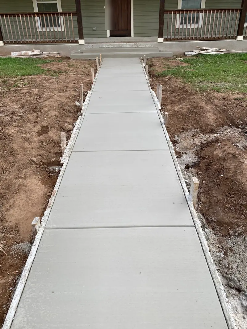 New concrete sidewalk running up to the front porch of a green house.