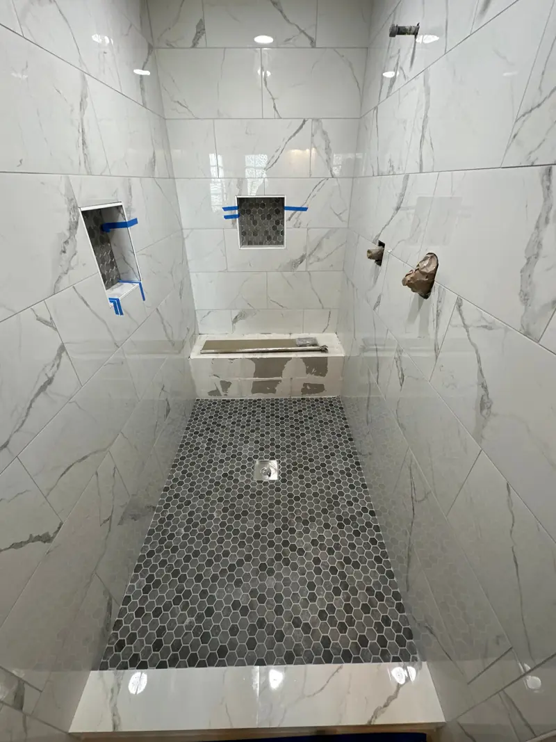 Walk-in shower with large white marble-look wall tile, two niches, a built-in bench and a gray hexagon mosaic floor.