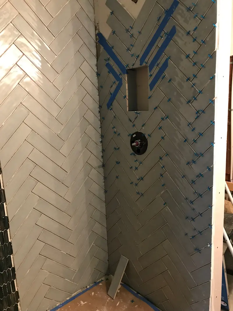 White tile going up in a herringbone pattern, with spacers still in the joints.