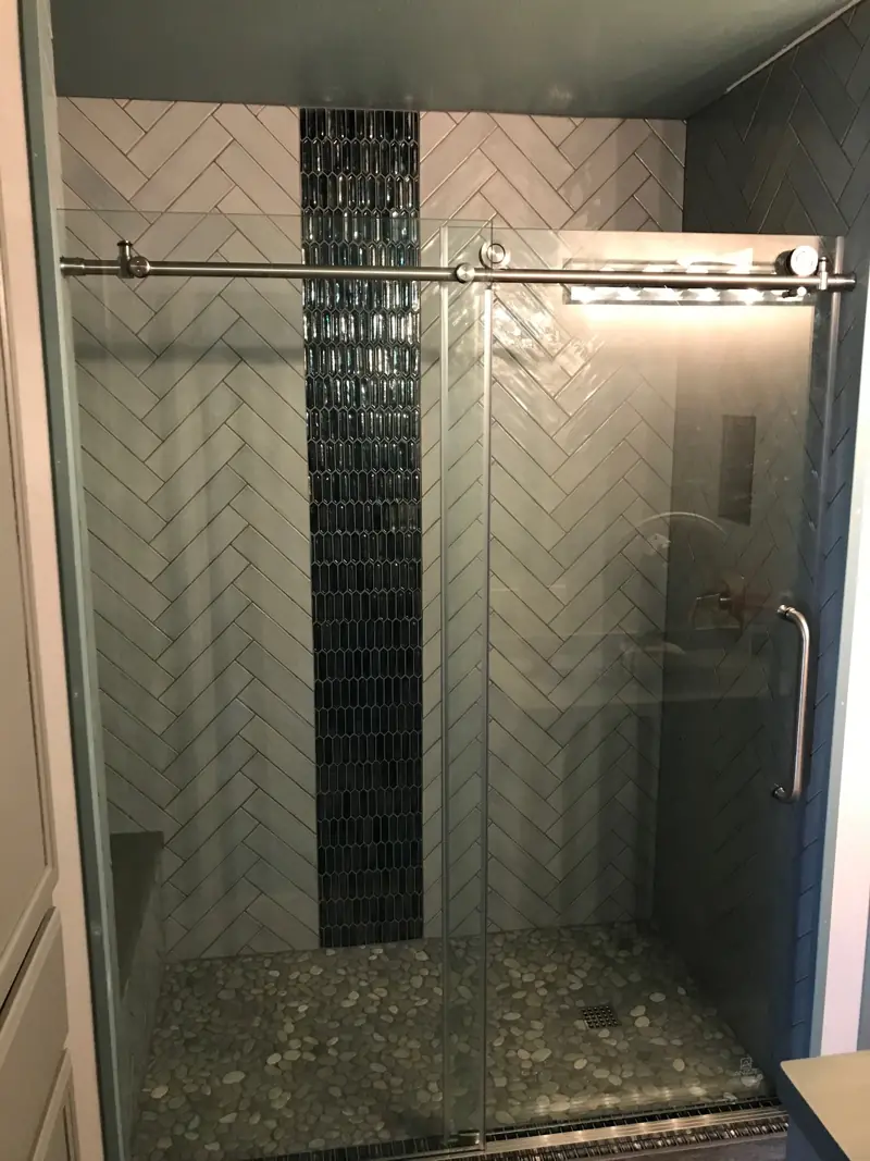 Finished shower with a sliding glass door, the blue mosaic stripe and a pebble floor.