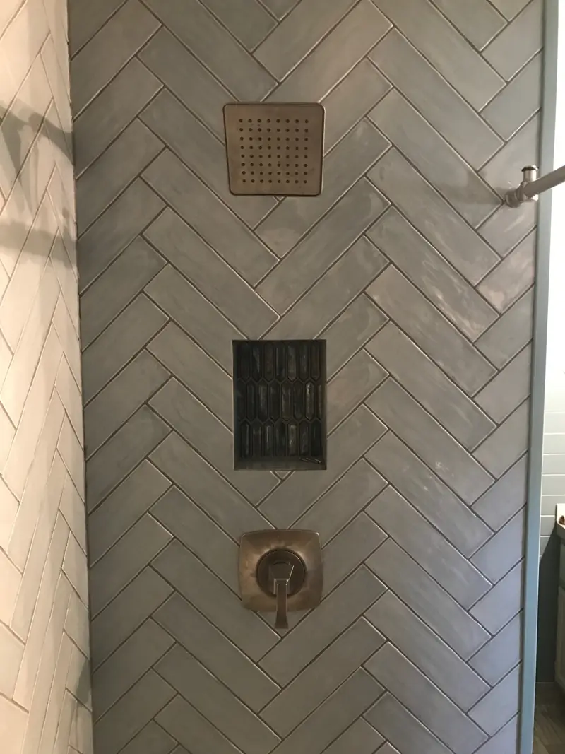 Square shower head, a tiled niche and the valve trim set in herringbone white tile.