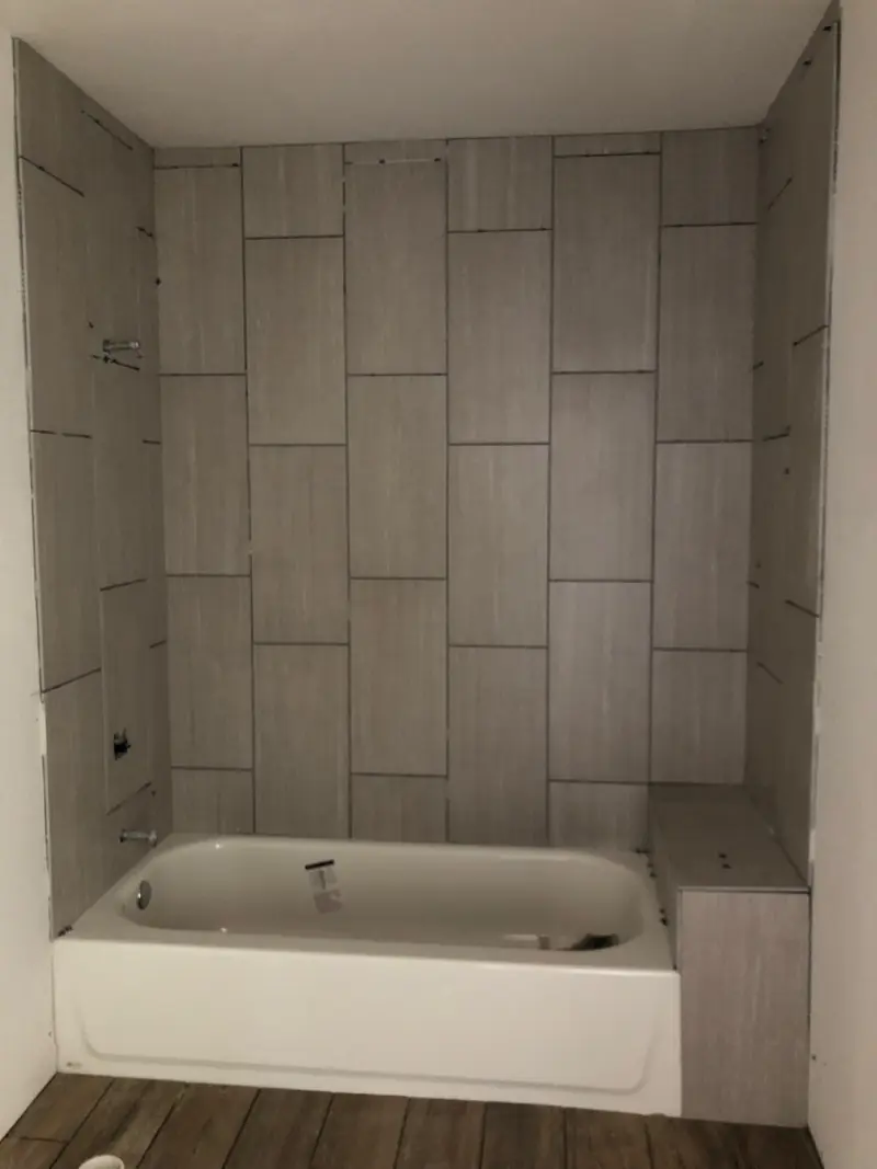 Bathtub surrounded by large gray plank tile laid in a stacked pattern.
